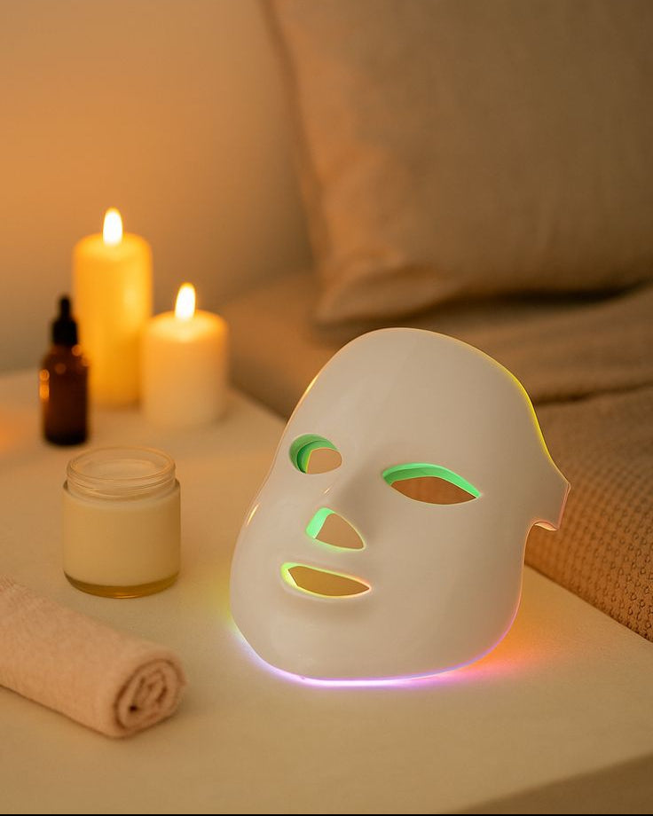 White facial mask light with colorful LED lights on a nightstand with candles and a pillow in the background.